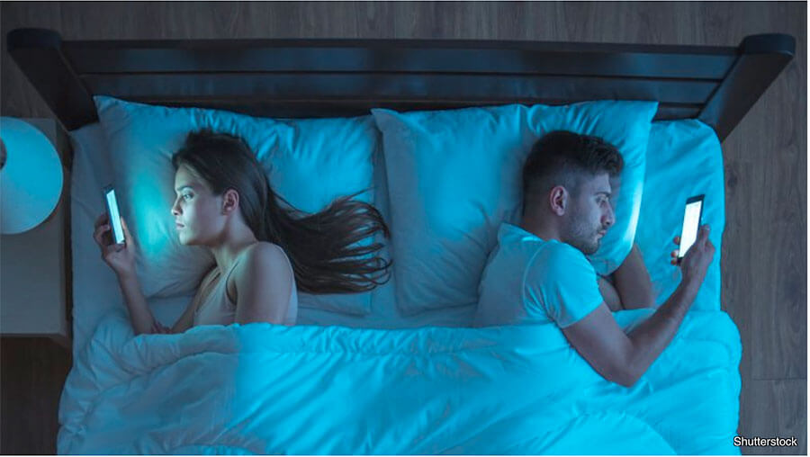 couple in bed both looking at phones
